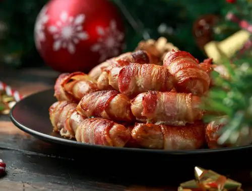 Christmas Pigs in blankets, sausages wrapped in bacon with decoration, gifts, green tree branch on wooden rustic table.